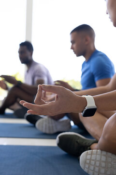 Diverse men meditating on blue mats in yoga studio, showing white smartwatch and sneakers