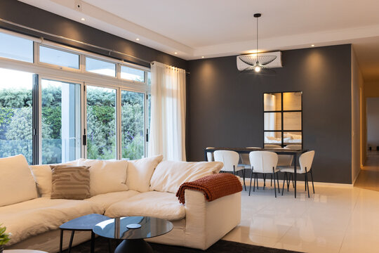 White L-shaped sectional sofa is anchoring open-plan living dining area with nested black tables