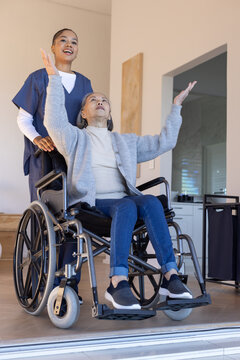 Carer in scrubs standing behind Senior woman sitting in manual wheelchair at doorway raising arms