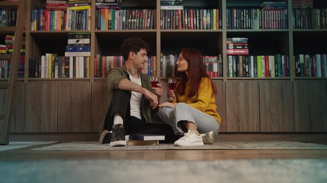 Young couple enjoying romantic date in home library while drinking wine