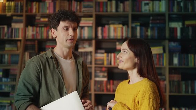 Male librarian talking with female colleague in bookshop about a new book