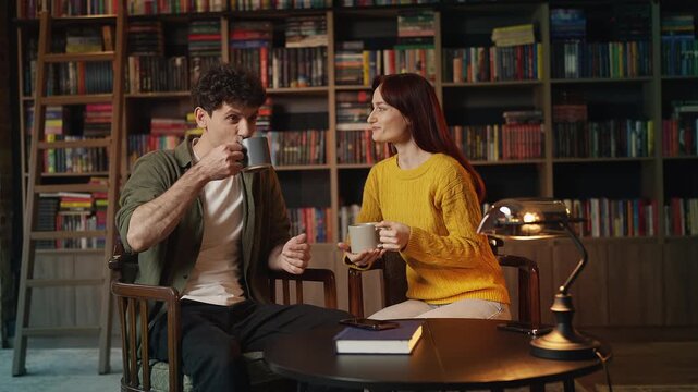 Happy red-haired woman and boyfriend drinking tea and talking in coffee shop