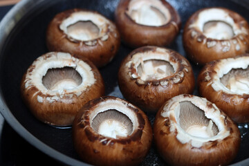 Fototapeta premium Fresh champignon mushrooms in a frying pan on a black background. Healthy eating concept.