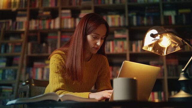 Focused female student doing academic research on laptop in university library
