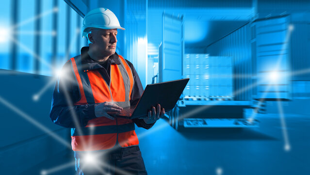 Logistics operations. Warehouse engineer manages cargo transportation and container shipments using laptop in modern distribution terminal.