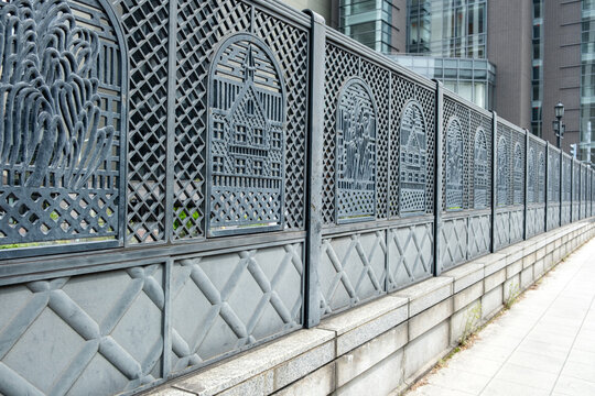 Gray cast metal fence with lattice relief panels by modern office sidewalk in Japan