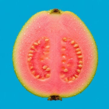 Macro shot of single fresh pink guava sliced in half with water droplets on bright blue background depicting juicy tropical fruit and natural sweetness