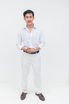 A young Southeast Asian man smiles warmly with a welcoming gesture, standing in a bright studio and conveying friendliness and approachability.