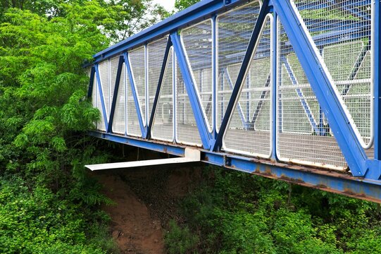 Blue steel truss bridge with unexpected structural defect and improvised metal patch as engineering flaw concept