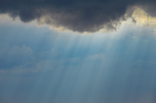 Dark cloud edges reveal soft Tyndall rays streaming beneath them, creating a calm and atmospheric sky scene.