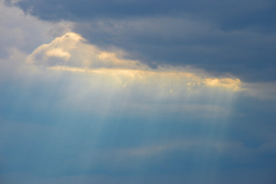 Sunbeams pierce through a drifting cloud, revealing a soft Tyndall effect as light scatters in the misty air.