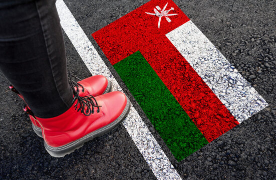 a woman with a boots standing on asphalt next to flag of Oman and border
