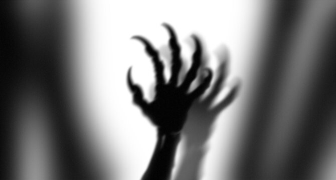 Scary monster hand with long sharp claws reaching out in the dark with bright dramatic light behind