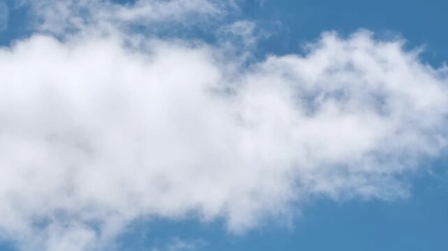 Soft white cumulus clouds drifting across a vibrant clear blue sky on a bright sunny day with natural light