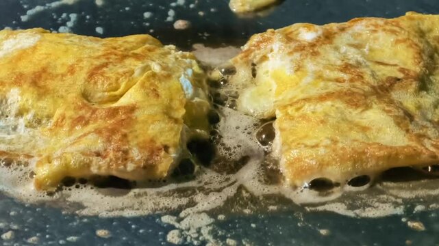 Delicious golden omelets sizzling and bubbling in a hot frying pan, actively cooking a fresh and savory breakfast or brunch meal