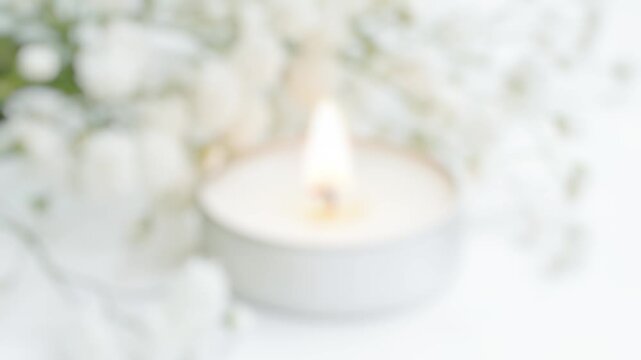 A simple yet elegant arrangement of white flowers sits next to a burning white candle