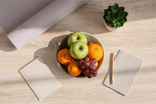 Healthy lifestyle concept with fresh fruit, yoga mat, and notebooks on a wooden table.