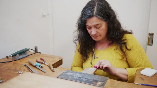 Woman goldsmith sawing a metal piece for jewelry making