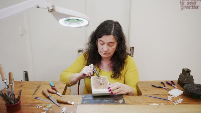 Professional artisan goldsmith soldering jewelry in her workshop