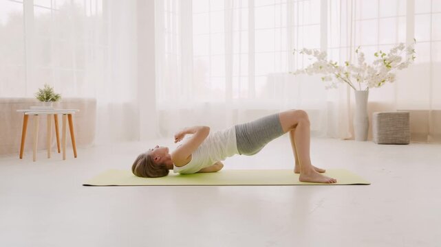 Side view of woman doing bridge exercise with back stretching on mat at home