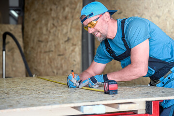 A worker measures wood structural panel (OSB) before cutting it to size. Dry construction of an...
