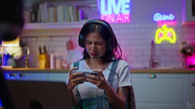 Asian young e-sport woman gamer play online mobile game on smartphone.Attractive girl vlogger influencer content creator gamer enjoy and fun live streaming broadcast games in POV screen and neon room.