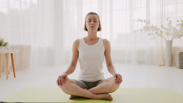 Woman with closed eyes doing breathing exercise on yoga mat at home
