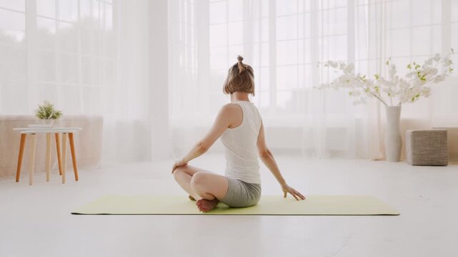 Side view of woman doing spinal spirals on yoga mat at home