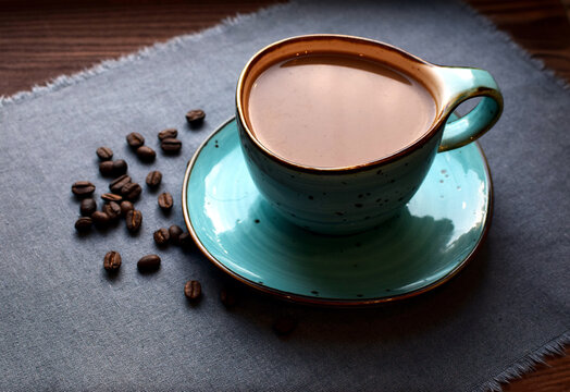 Coffee with milk in a beautiful blue ceramic cup on a wooden table. Cup of coffee, coffee beans.
