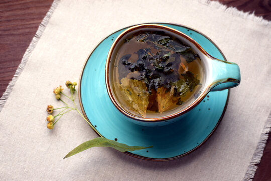 Herbal green tea with dried ginkgo biloba leaves and linden in a blue ceramic cup on a cloth napkin.