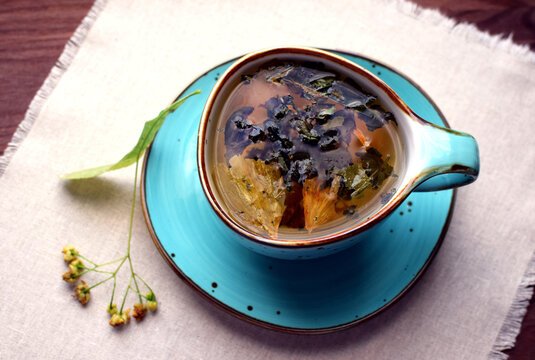 Herbal green tea with dried ginkgo biloba leaves and linden in a blue ceramic cup on a cloth napkin.