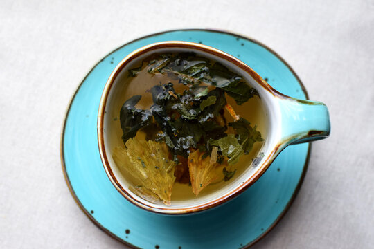 Herbal green tea with dried ginkgo biloba leaves and other dried herbs in a blue ceramic cup on a fringed cloth napkin.