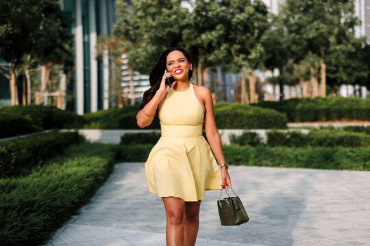 Professional woman having a phone conversation outdoors in a modern city park on a sunny day, representing communication and urban lifestyle