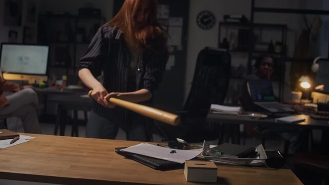 Stressed Caucasian young adult woman smashing digital clock with baseball bat on desk while working late. Clip perfect for projects on workplace burnout, stress, and mental health awareness