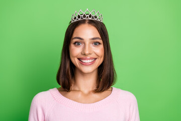 Beautiful young woman with tiara smiles on bright green background wearing pink sweater perfect for fashion glamour lifestyle and festive promotion © deagreez