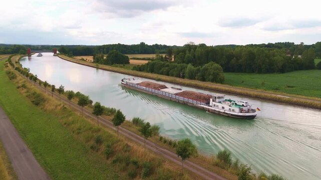 Industrial cargo barge cruising on river canal, aerial view of freight ship transporting goods, commercial waterway logistics in rural landscape