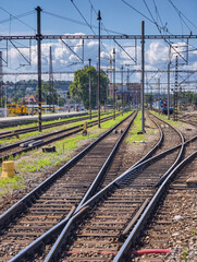 Fototapeta premium Railway junction with multiple tracks converging and branching under an electrified overhead system. Steel poles switches and crossings highlight the technical complexity of modern rail infrastructure