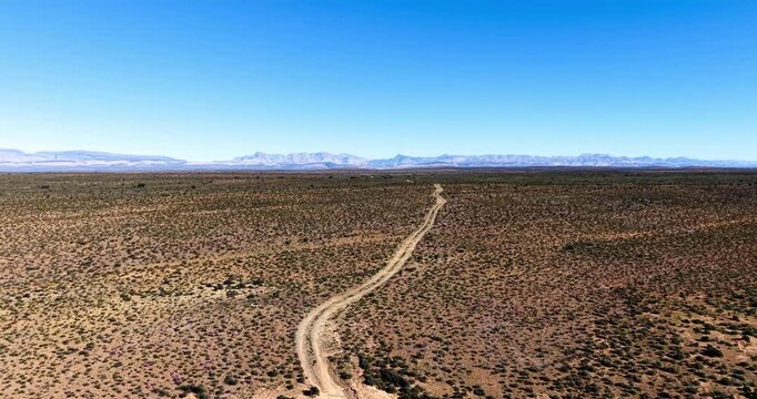 Expansive aerial view of the Great Karoo near Prince Albert, showcasing rugged terrain, indigenous shrubs, a winding gravel road and dramatic mountain backdrop in the Western Cape