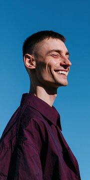 Smiling young man in burgundy shirt against clear blue sky portrait for outdoor banner and lifestyle profile design