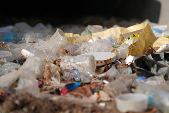 Plastic waste garbage pollution landfill recycling litter cup bottle scattered across dump site, close up debris in sunlight, highlighting environmental damage and cleanup urgency