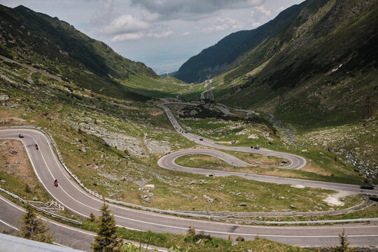 Aerial view of a spectacular winding mountain road, known for its challenging curves, nestled between green, rocky slopes under a cloudy sky. Perfect for road trips and adventure travel.
