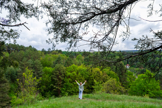 Person raising hands wide open facing vast green forest landscape framed by pine branches. Freedom, connection with nature, and environmental protection concept.