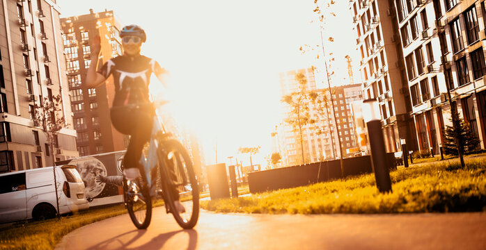 Blurred motion of female cyclist waving hand on bicycle track at sunset. Dynamic cycling, active lifestyle concept, speed motion.