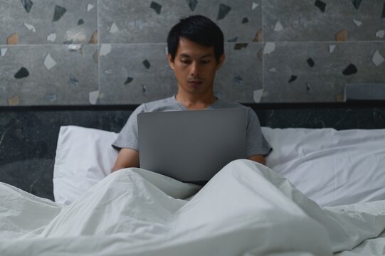 Man Working on Laptop in Bed at Night with Cozy Bedding Surroundings