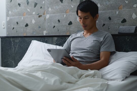 Young Man Relaxing in Bed While Using a Tablet Device at Home