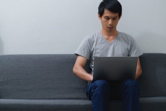 Young Man Working on Laptop While Sitting on Gray Couch at Home