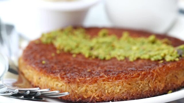 Close up video showcasing kunafa a traditional middle eastern dessert garnished with vibrant green pistachios on a white plate