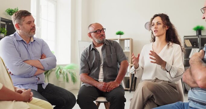Adults group therapy counseling discussion support meeting. Adults sit in a circle as a facilitator leads session on feelings, communication, trust and respect. Clear concept of people support.