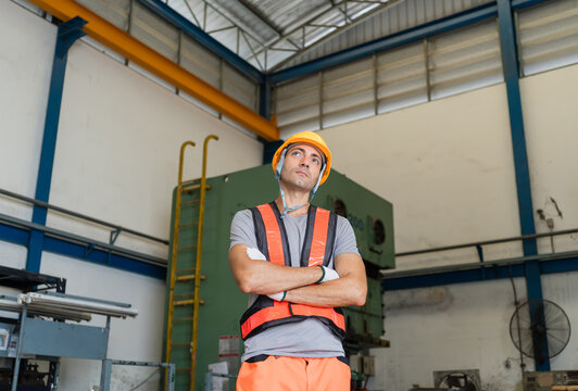 worker in hi-vis vest gazing upward beside tall power press machine