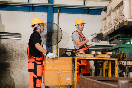 Worker inspecting metal bracket near industrial press die with colleague